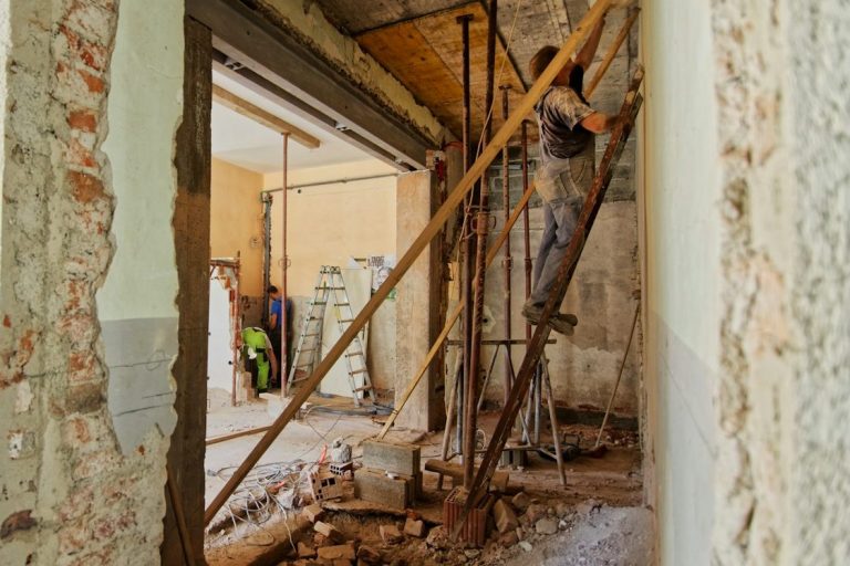 Altbausanierung Bauarbeiter repariert Wände mit Gerüst und Werkzeug in einem renovierungsbedürftigen Raum.